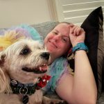 Jodie laying on a grey couch with Wally laying in front of her both smiling